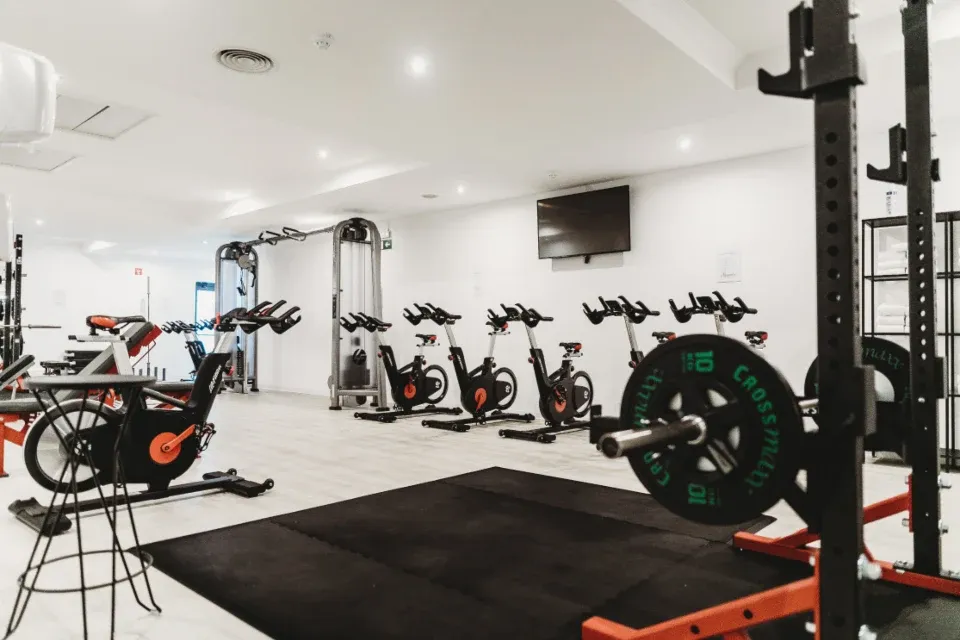 A bright gym with bikes, a squat rack and rubber flooring